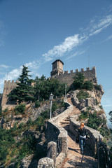 Fototapeta premium Woman dressed in a motorcycle outfit and sunglasses. body protection turtle and knee pads, helmet in hand. Fortress, stone steps, stairs. Vertical photo. Pass of the witches San Marino