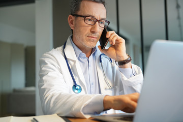 Doctor in office working on laptop talking on phone
