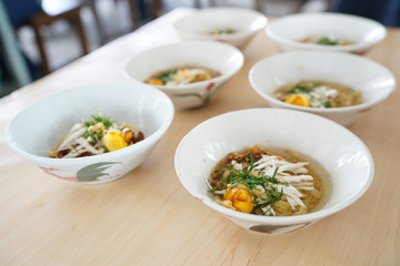 A bowl of spicy Thai noodle soup with chicken and boiled egg also known as tom yum on wooden background, Traditional Thai food recipe, Popular street food of Thailand.