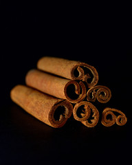 Close-up of cinnamon sticks laid on top of each other by a triangle on a black blurred background