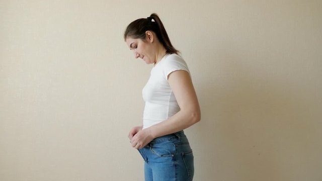 A plump young woman tries to button her jeans. Side view.