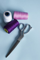 Silver scissors with pink white violet sewing threads on blue pastel background