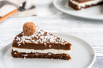 piece of chocolate cake on a plate. Chocolate and coconut cake on a white wooden background. Foodfoto in a high key. Raw dessert
