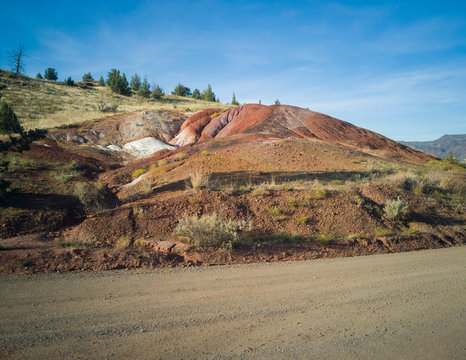 Unique red and white clay hill with a trees and a sky in the background and the road in the foreground at the John Day Fossil Beds Painted Hills Unit in Mitchell Oregon