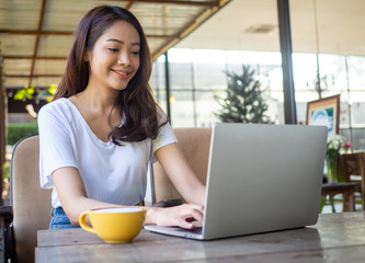 Fototapeta premium Asian woman pretty face wearing a white shirt, sitting and working in a coffee shop.