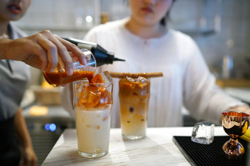 Pouring iced tea latte into a glass of fresh milk on blurred background, Mix of Thai black tea and...