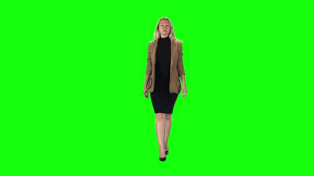 Blonde girl in a stylish brown jacket, black dress and high-heeled shoes going against a green screen. Slow motion