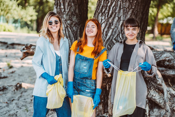 Friends picking up trash from the park. They collecting the litter in garbage bag