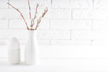 White vase with willow branch , white egg and cups on a white table Copyspace