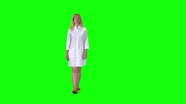 Blonde girl in a white medical coat going against a green screen. Slow motion