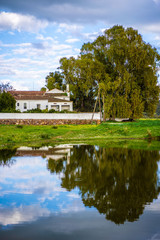 Fototapeta na wymiar Casa de campo junto a un lago y árboles con cielo nublado