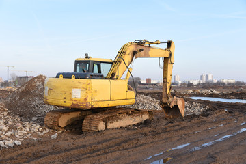 Obraz premium Yellow excavator during groundwork on construction site. Hydraulic backhoe on earthworks. Heavy equipment for demolition, construction and ground works. Digging foundation and laying storm sewer pipes