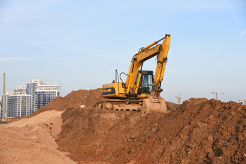 Yellow excavator during groundwork on construction site. Hydraulic backhoe on earthworks. Heavy equipment for demolition, construction and ground works. Digging foundation and laying storm sewer pipes