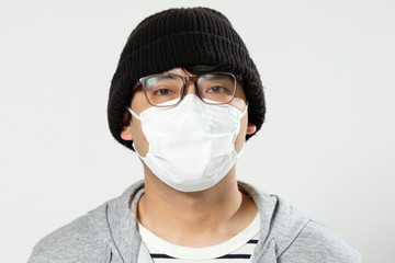 感染症予防の為に衛生マスクをしている眼鏡をかけてニット帽をかぶってる日本人男性のバストアップ正面