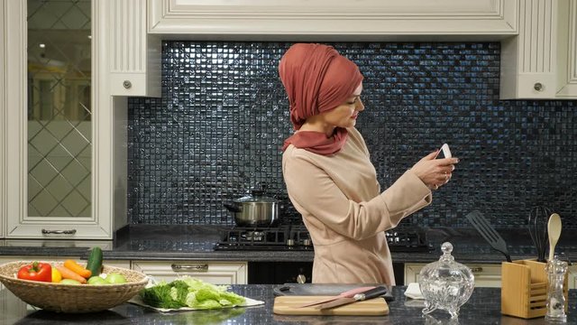 pretty oriental lady in hijab stands half face and makes selfie against fresh organic food on table close-up