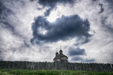 Old wooden church behind a large wooden picket fence against dramatic sky