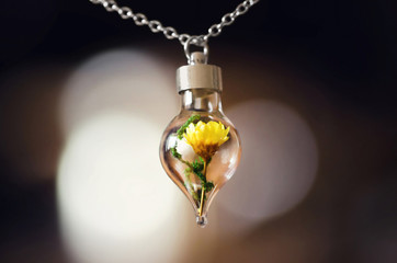 Pendant made with drop-shaped glass bottle with tiny yellow flower inside