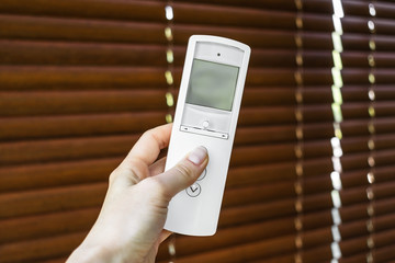 remote control for blinds. female hand holds and directs a remote control on wooden shutters to open it