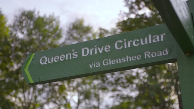 Medium low angle still shot of a wooden green direction signpost pointing to Queen's drive via Glenshee Road, Braemar, Aberdeenshire, Scotland, UK