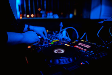 Club DJ playing mixing music on vinyl turntable at party wearing sunglasses with lens flare from...