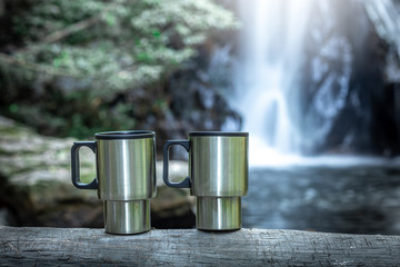 Close up two iron coffee mug on wood with the waterfall behind.