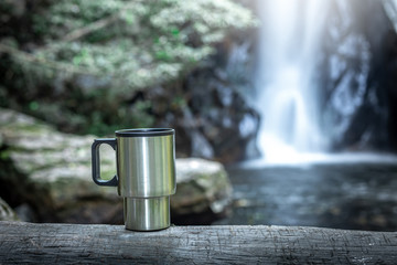 Close up iron coffee mug on wood with the waterfall behind.