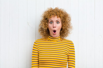 young pretty woman looking very shocked or surprised, staring with open mouth saying wow