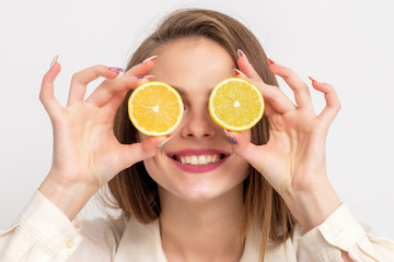 Smiling woman covering eyes with halves of fresh ripe orange fruit, close up.