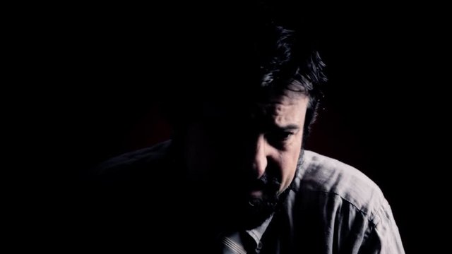 Artistic shadowy shot: a self-denigrating man's expression. Close-up shot of the face. Part of a series of depictions of feelings and emotions with professional actors.