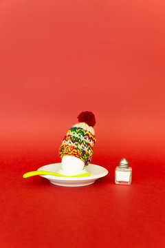 Fun breakfast concept with a boiled egg wearing a knitted woolen hat on red background.