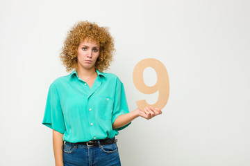 young pretty afro woman sad, depressed, unhappy, holding a number 9.