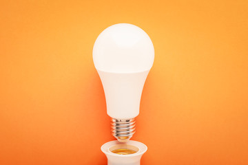 LED lamp twisted out of a socket on an orange background: energy-saving concept and the hour of the...