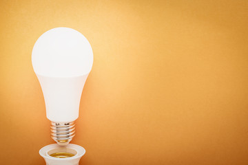 LED lamp twisted out of a socket on an orange background with copy space: energy-saving concept and Earth Hour