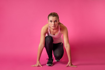 Fit woman on pink background at starting position ready for sprint