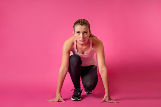 Fit woman on pink background at starting position ready for sprint