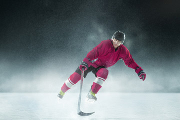 Leader. Male hockey player with the stick on ice court and dark background. Sportsman wearing equipment and helmet practicing. Concept of sport, healthy lifestyle, motion, movement, action.