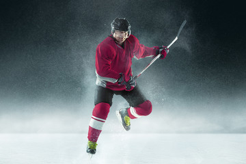 Attacking. Male hockey player with the stick on ice court and dark background. Sportsman wearing...