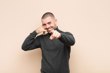 young handsome man smiling cheerfully and pointing to camera while making a call you later gesture,...