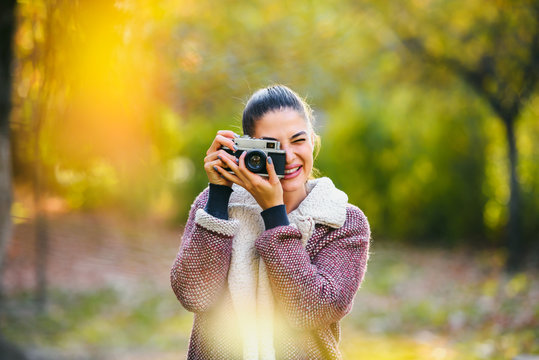 Portrait of beautiful young woman taking photos with vintage camera outdoors in the nature