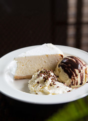 A slice of cheese cake with ice cream and whipped cream on a white plate.