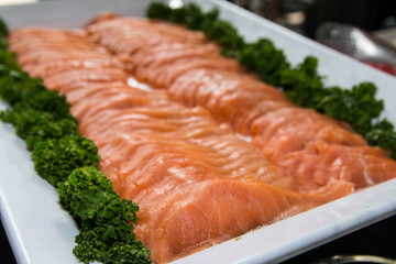 Fresh raw salmon being served on a white tray with vegetables decoration.