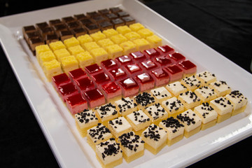 Mini slice colorful cakes with a lot of flavors on a white tray.Small bites cakes in a party buffet.