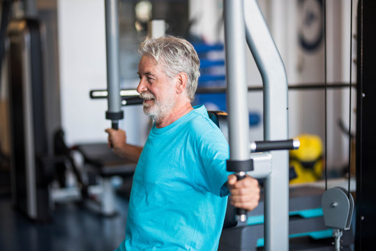 close up of mature man at the gym doing exercise alone lifting weight to build his body and be fit - active pensioner senior training hard and holding the machine of the gym