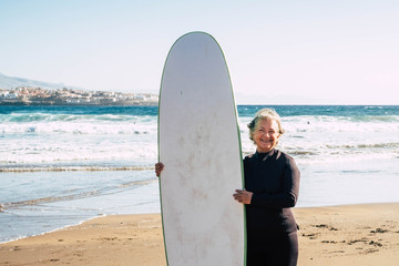 one mature woman with a surftable and wetsuit having fun at the beach smiling and having fun -...