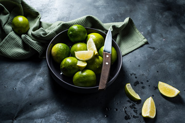 Fresh ripe limes and knife in black bowl. Sliced. Dark, metal background. 