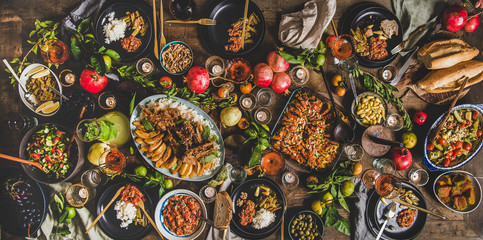 Flat-lay of Turkish traditional foods sush as lamb chops, quince, green beans, vegetable salad, babaganush, rice pilav, pumpkin dessert, lemonade over rustic table, top view. Middle East cuisine