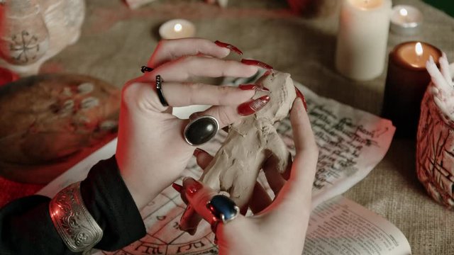 Cropped view of witch with rings sticking needle in voodoo doll