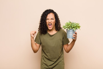 young black woman shouting aggressively with an angry expression or with fists clenched celebrating...