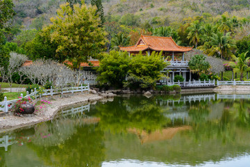 Fototapeta na wymiar Green lake surrounded by gazebos, temples, mountains, flowers, palm grove and stone fence on the territory of Buddhist center Nanshan.
