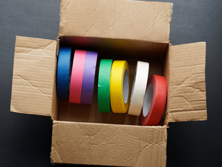 Rolls of colored masking tape in a carton box.